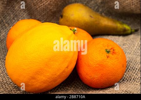 limone, tangerini e pera su uno sfondo di tessuto omespun ruvido. Primo piano Foto Stock