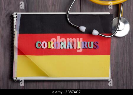 Testo Coronavirus in Germania da lettere in legno, taccuino, stetoscopio sullo sfondo con bandiera italiana Foto Stock
