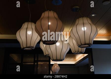 Primo piano di lampade retrò con paralumi geometrici appesi sotto il soffitto. Superficie in tessuto beige di lanterne cinesi tradizionali con luce brillante Foto Stock