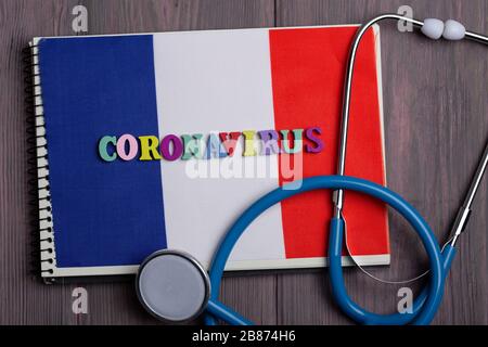 Testo Coronavirus in Francia da lettere in legno, taccuino, stetoscopio sullo sfondo con bandiera italiana Foto Stock