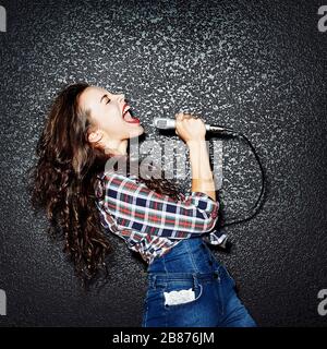 Karaoke party. È il momento di cantare! Pazzesco casual riccio chic ragazza cantare con il microfono. Studio Foto Stock