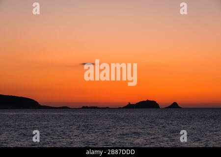 Bagliore arancione come il sole tramonta dietro una 'la pietra' argentata, la roccia rossa a Ile Rousse nella regione Balagne della Corsica Foto Stock