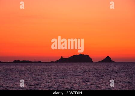 Bagliore arancione come il sole tramonta dietro una 'la pietra' argentata, la roccia rossa a Ile Rousse nella regione Balagne della Corsica Foto Stock