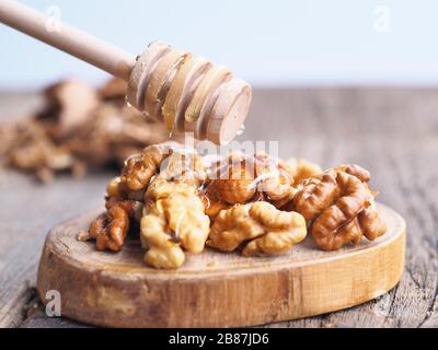 Noccioli di noce con salsa di miele in cima, macro colpo isolato su un tagliere di legno e tavolo legnoso come sfondo. Messa a fuoco selettiva Foto Stock