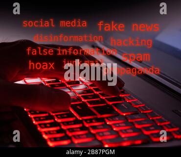 Primo piano delle dita digitare al buio i tasti di retroilluminazione rossi illuminati sulla tastiera del computer. Testo rosso brillante su computer hacker, notizie false, disinf Foto Stock