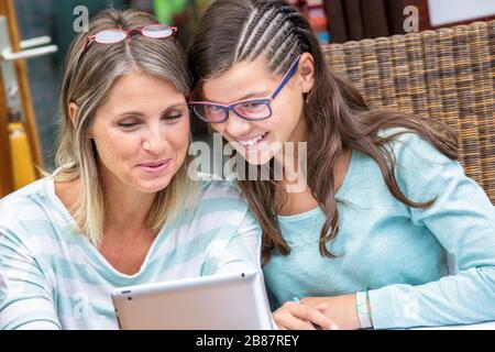 ragazza allieva sorridente che fa i compiti sul tablet con l'insegnante bella di mezza età Foto Stock