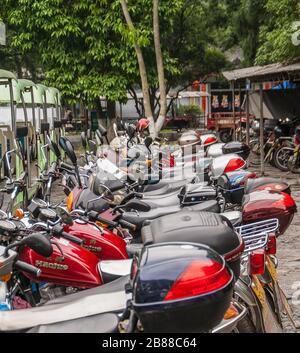 Guilin, Cina - 10 maggio 2010: Centro città. Parcheggio sotto alberi verdi pieno di linee di moto in diversi colori. Foto Stock