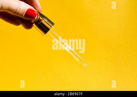 Pipettare con liquido gualinico in una mano femmina. Siero con particelle d'oro per la pelle. Spazio di copia per il testo Foto Stock