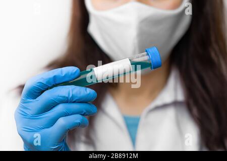 Provetta con vaccino contro il coronavirus, 2019-nCoV, SARS-nCov, COVID-19 in maschera protettiva e guanti blu per scienziato. Foto Stock