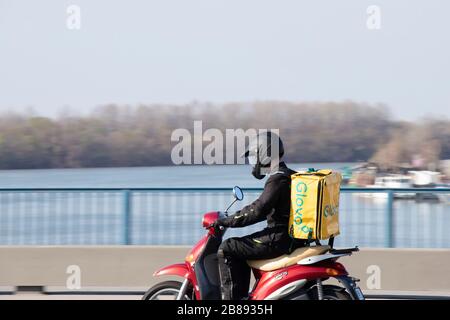 Belgrado, Serbia - 18 marzo 2020 : UN corriere che lavora per il servizio di consegna di cibo Glovo a bordo di una moto scooter sul ponte sul fiume Sava Foto Stock