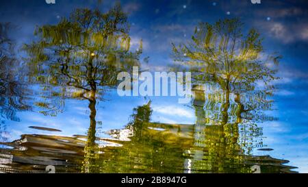 Riflessioni in pozzanghere o lago di edifici, barca o alberi e lampade da strada. Foto Stock