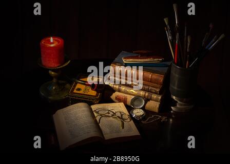 Una vecchia scrivania con un mucchio di libri di pelle marrone vintage, un libro aperto con occhiali, una tazza di caffè, una candela rossa con fiamma, un blocco tasca vintage Foto Stock