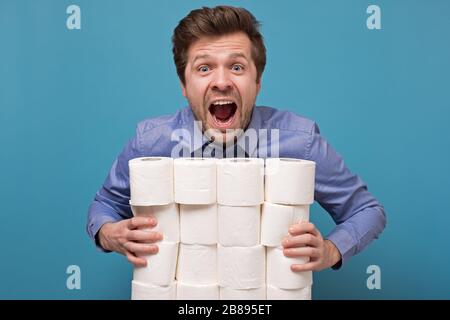 Eccitato felice uomo caucasico che tiene un mucchio di carta igienica isolato su sfondo blu. Studio Foto Stock