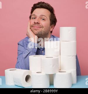 Eccitato felice uomo caucasico in possesso di una pila di carta igienica che mostra pollice isolato su sfondo rosa. Studio Foto Stock