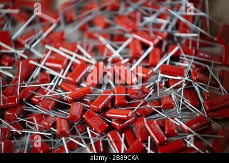 Il primo piano di un gruppo di condensatori rossi si trova l'uno sopra l'altro in una fabbrica di computer e apparecchiature per ufficio. Concetto di parti di qualità. Lotto all'ingrosso Foto Stock