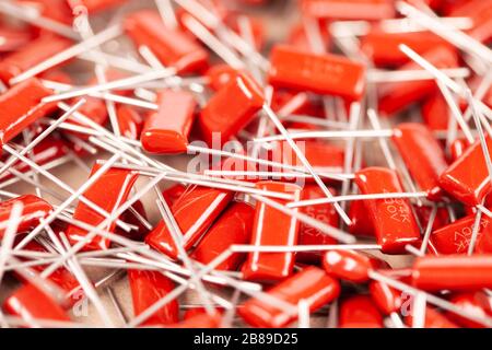 Il primo piano di un gruppo di condensatori rossi si trova l'uno sopra l'altro in una fabbrica di computer e apparecchiature per ufficio. Concetto di parti di qualità. Lotto all'ingrosso Foto Stock