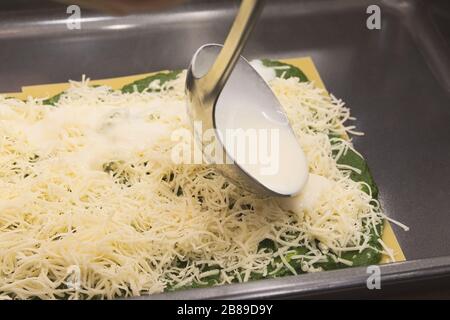 Salsa cremosa bianca con mestolo su lasagne di spinaci crudi Foto Stock