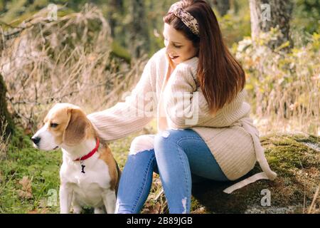 Giovane donna sorridente, seduta accanto al suo cane durante una passeggiata Foto Stock