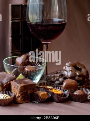 Un bicchiere di vino rosso è circondato da una varietà di tutto il cioccolato, bar, biscotti, torta e pezzi di fantasia ripieni Foto Stock
