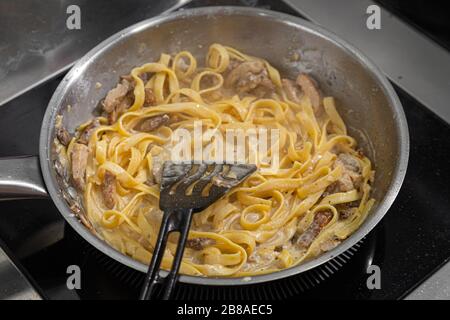 primo piano chef maschio frigge grandi gamberi re e pasta in olio d'oliva in una padella di metallo. Il processo di preparazione della pasta ai gamberi Foto Stock