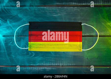 Maschera medica per la protezione contro le malattie aeree, dipinta sulla bandiera nazionale della Germania su sfondo nero con fumo blu-verde. Pro. Medico Foto Stock