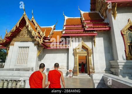 Due monaci buddisti con le rose arancioni che entrano nel punto di riferimento Wat Benchamabophit (conosciuto anche come Tempio di marmo) a Bangkok, Thailandia Foto Stock