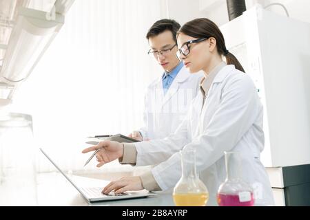 Giovane ricercatore scientifico femminile che presenta il nuovo virus al suo collega e ne descrive le caratteristiche in laboratorio Foto Stock