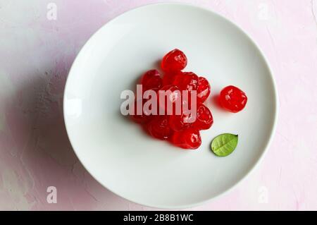 Ciliegie candite su piatto bianco isolato su fondo rosa. Vista dall'alto. Foto Stock