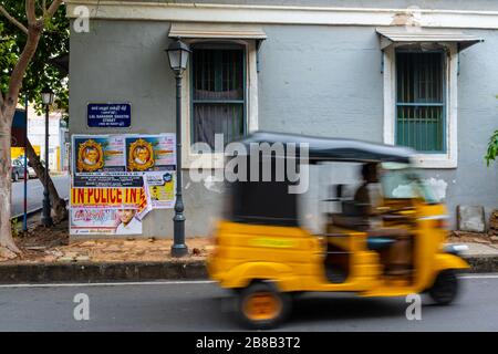 Pondicherry, India - 17 marzo 2018: Uomo irriconoscibile in un risciò che passa di fronte ad un muro grigio e cartello stradale e manifesti con movimento sfocato Foto Stock