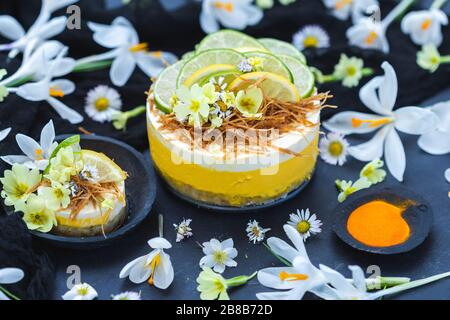 Torta vegana cruda con limone e lime su un nero superficie ricoperta da minuscoli fiori a margherita Foto Stock