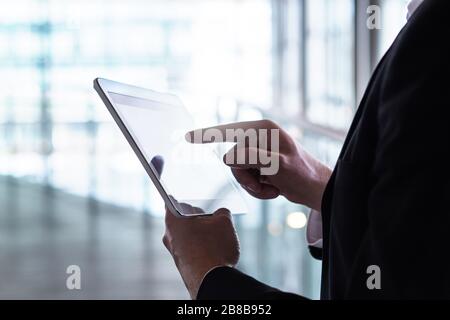 Uomo in tuta con tablet. Uomo d'affari con dispositivo mobile intelligente in un moderno edificio in vetro. Foto Stock
