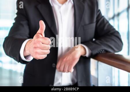 Uomo d'affari o avvocato che dà i pollici in su nell'edificio moderno dell'ufficio. Buon uomo d'affari che mostra un gesto di mano soddisfatto e di supporto. Foto Stock