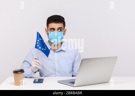 Uomo pensoso in maschera igienica e guanti che tengono bandiera UE, preoccupato e ponderato, meditando per risolvere il problema del coronavirus, Covid-19 epidemia anx Foto Stock