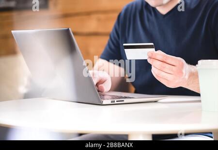 Uomo che detiene la carta di credito e che digita le informazioni bancarie o i numeri di identificazione con il computer portatile. ECommerce e concetto di shopping online. Foto Stock