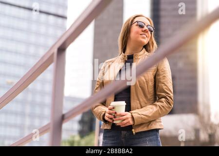 Una donna felice e rilassata che si diverte gustando una tazza di caffè da asporto in strada. La signora ha una pausa caffè in centro. Persona turistica o d'affari. Foto Stock