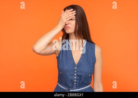 Facepalm. Afflitta donna bruna in denim vestire faccia con mano, sensazione di vergogna e dolore per la sconfitta, emozioni disperate. Indoo Foto Stock