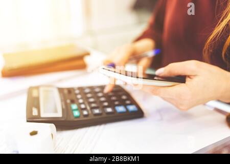 La donna d'affari lavora a casa, lavora a distanza a casa, con notebook e blocco note, prende appunti al telefono, conta su una calcolatrice. Primo piano di contabilità femminile o banchiere che fa calcoli. Concetto di risparmio, finanze ed economia Foto Stock
