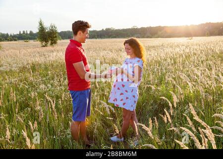 Una bella immagine all'aperto di un giovane che dà un regalo alla sua moglie incinta.incinta foto di famiglia in natura Foto Stock