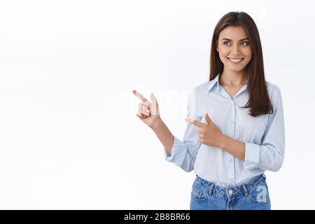 Splendida giovane donna adulta in blusa blu introdurre la sua azienda banner, amichevole e felice sorridente, puntando a sinistra a vuoto spazio bianco per Foto Stock