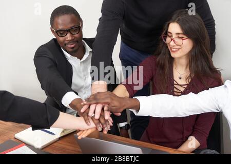 Giovani uomini d'affari felici che lavorano insieme in un ufficio moderno, lavoro di squadra multietnico. Partner commerciali che fanno un mucchio di mani in riunione Foto Stock