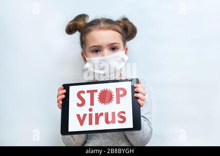 Una bambina in una maschera medica mostra la compressa con le parole STOP VIRUS. Protezione contro l'epidemia di coronavirus Foto Stock