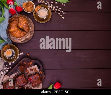 Colazione di Pasqua con espresso fresco aromatico, croissant, torta al brownie, uova colorate, tulipani rossi e salice. Caffè con pasticcini, fiori su un tavolo di legno. Sopra. Foto Stock