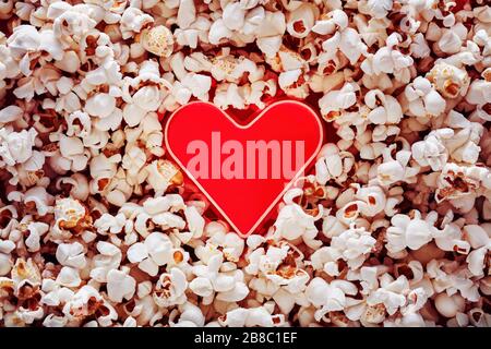 Forma del cuore in un mucchio di popcorn con spazio di copia. Guardare film romantici durante il giorno di San Valentino. Vista dall'alto. Foto Stock