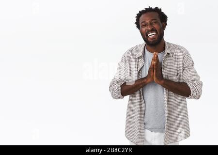 Spensierato, felice e riconoscente uomo afro-americano sorridente con barba, acconciatura afro, si aggrada le mani insieme in preghiera e ridendo mostrando gratitudine Foto Stock