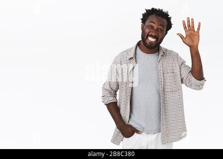 Amichevole uscente afro-americano bearded guy, alzare la palma e agitare la mano come dire ciao o hi, sorridendo salutarvi con allegro, entusiasta Foto Stock