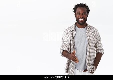 Piacere di conoscarla. Allegro afro-americano bearded ragazzo stretch braccio per stretta di mano per salutare qualcuno, sorridendo amichevole, dicendo ciao, guardando uscente Foto Stock