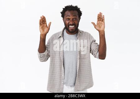Simpaticissimo e spensierato fallo afro-americano con espressione divertente ed entusiasta, giocando con il capretto peekaboo, alzando le mani in su, sorridendo e. Foto Stock