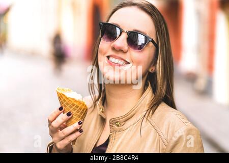 Gelato sul viso sudicio. Buona donna ridente che mangia il gelato in città che si scioglie e gocciola. Foto Stock