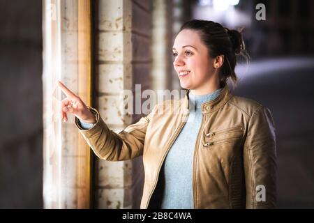 Donna finestra shopping. Shopaholic ammirare e sognare nuove scarpe, borse o vestiti. Donna sorridente che punta il vetro del negozio di moda con il dito. Foto Stock