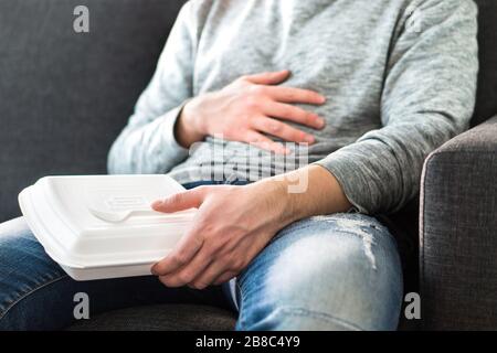 Dopo aver mangiato fast food. L'uomo si sente pieno o prende il pisolino dopo aver mangiato la roba di rifiuto. Tipo che ha hangover o dieta non sana. Mal di stomaco mentre si è seduti sul divano. Foto Stock